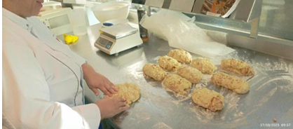 L'image montre une scène d'un atelier pratique de pâtisserie. L'enseignante de la délégation française, vêtue d'un uniforme de cuisine, façonne des pâtons de pâte, prêts à être cuits. L'atelier est bien équipé avec des surfaces de travail propres et des outils de pâtisserie professionnels.