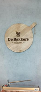 Cette photo montre un panneau indiquant la boulangerie d'application, simple, en bois et qui représente le logo de la boulangerie avec l'inscription « De Bakkers ».