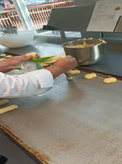 Cette photo montre l'enseignante de la délégation française, en train de préparer des biscuits sur une plaque de cuisson dans le laboratoire de pâtisserie. Elle utilise une poche à douille pour former des petites portions de pâte sur la plaque, sous une lumière naturelle et dans un environnement de travail propre et moderne. 